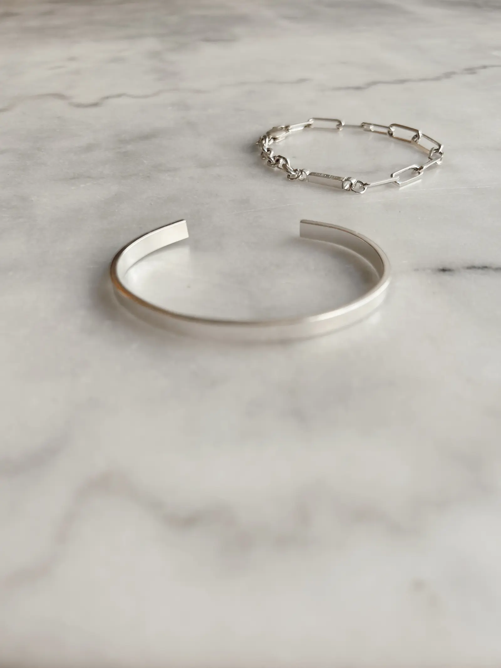 The Refined Arm cuff och ett länkarmband bredvid varandra på marmor
