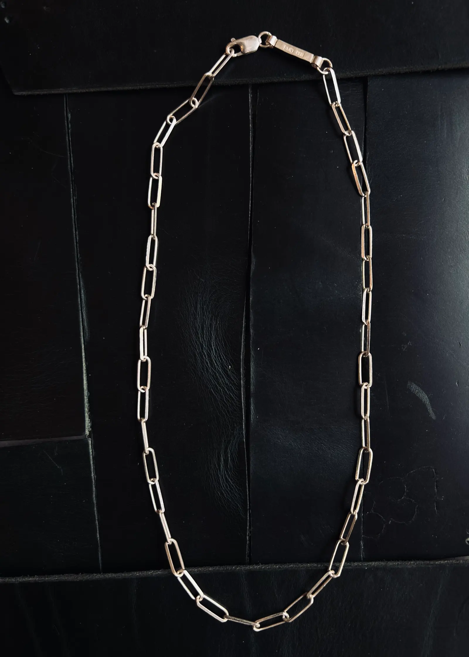 The Given Necklace utlagt på svart trä, de avlånga länkarna syns