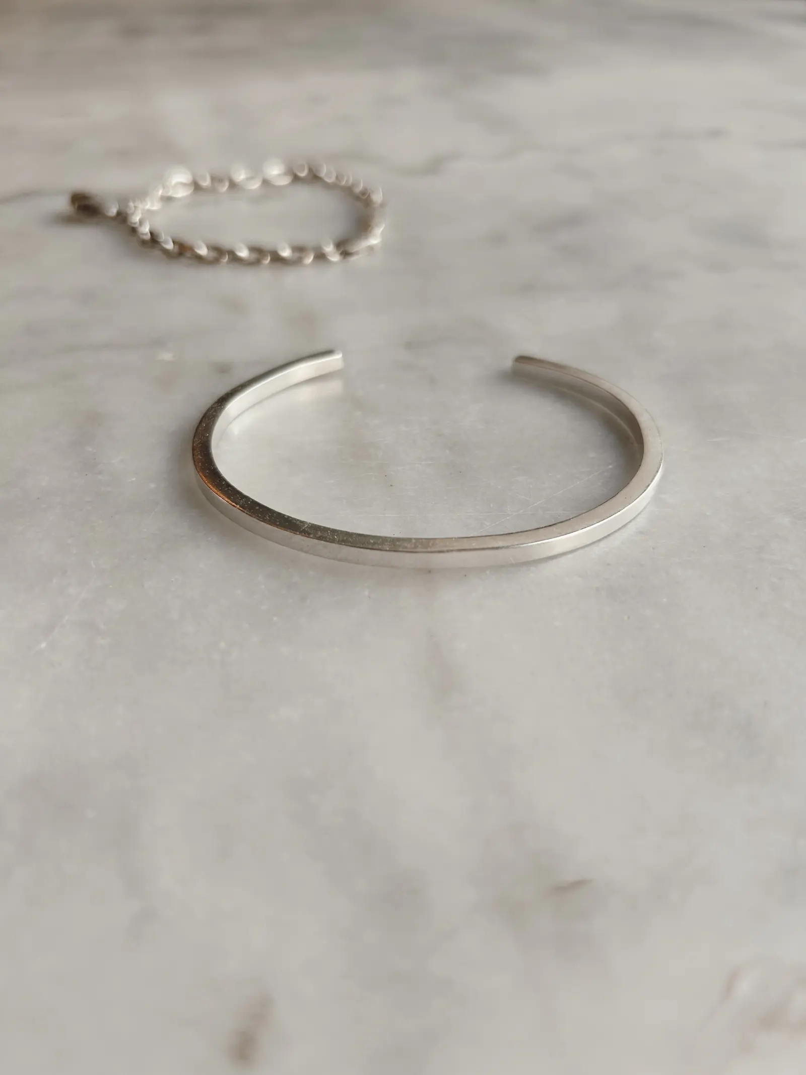 The Tidy Arm cuff och ett kedjearmband bredvid varandra på marmor